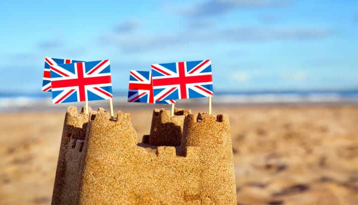 Picure of a sandcastle on a beach with two union jack flags on top.