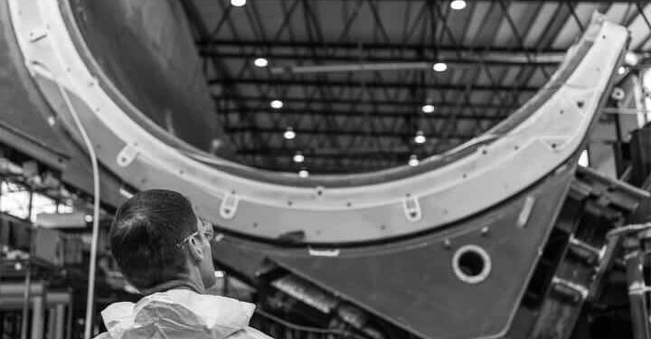 Black and white picture of a man looking up to a wind turbine blade mould.